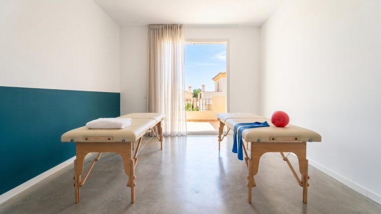 Dos camillas de tratamiento en una sala de fisioterapia luminosa con detalles en color teal