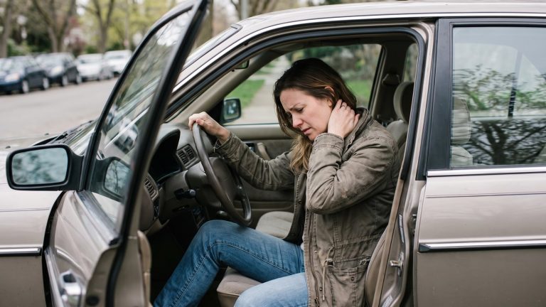 Mujer sentada en el asiento del conductor con la puerta abierta llevándose la mano a la nuca