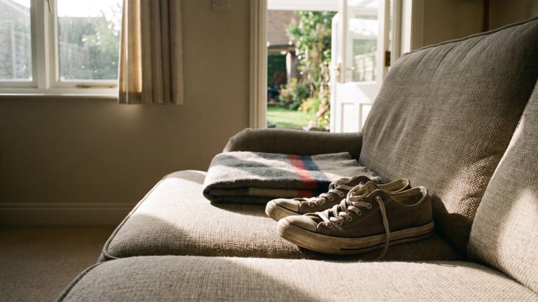 Zapatillas y una manta doblada sobre un sofá vacío en un salón iluminado por el sol