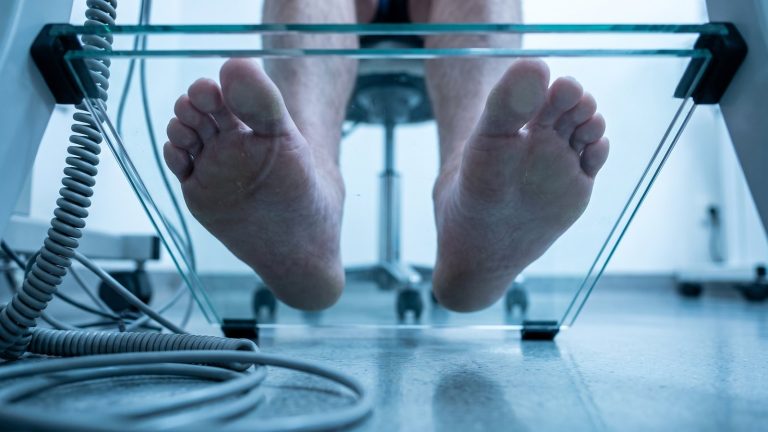 Vista inferior de dos pies descalzos apoyados sobre una plataforma de presiones de cristal